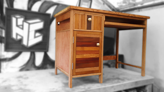  A Bespoke wooden desk, made from a combination of different woods. It has a cupboard with a drawer above it on the left and a keyboard drawer on the right.