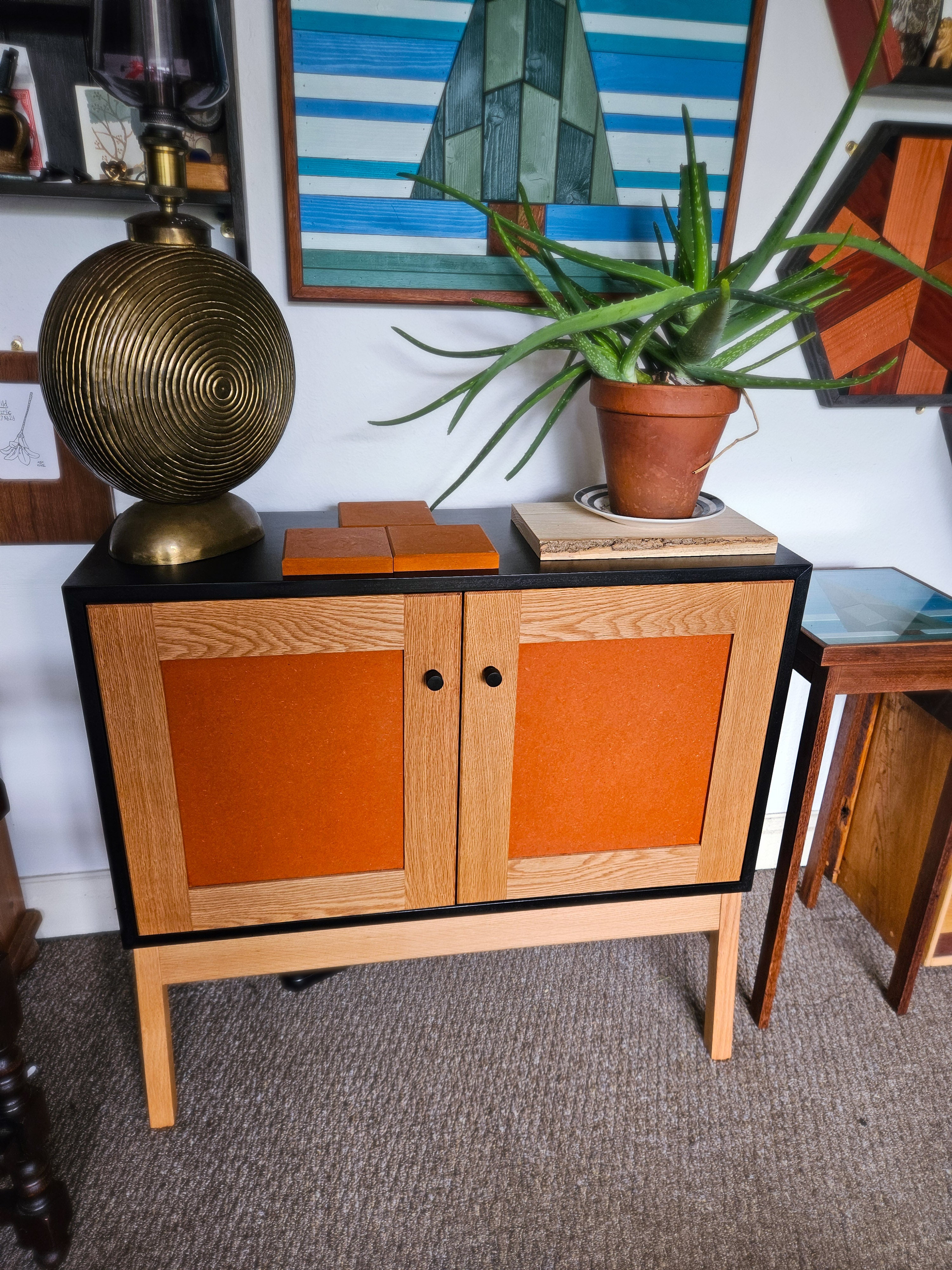 Wooden cabinet with orange doors in a room with decor elements like a plant and lamp.